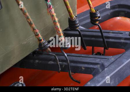 Gros plan du cordon élastique jaune altéré avec crochet en métal noir fixant la cargaison. Cette corde extensible solide maintient fermement l'équipement sur la plate-forme texturée du camion f Banque D'Images