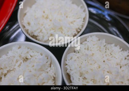 Gros plan vue de dessus de trois simples bols blancs de riz cuit moelleux. portion de nourriture chaude de la farine de céréales de base prête à être consommée, représentant réconfortant Banque D'Images