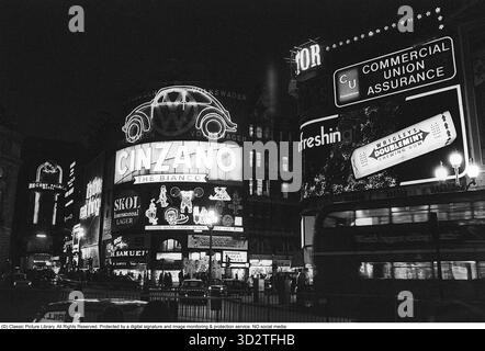 Piccadilly Circus dans les années 1970 Les emblématiques publicités éclairées de la zone éclairent les bâtiments environnants. Les panneaux publicitaires électriques sont une caractéristique déterminante de Piccadilly Circus depuis 1908, lorsque le premier affichage lumineux a été installé. Dans les années 1970, la zone était enflammée par des néons colorés et des enseignes incandescentes de marques telles que Coca-Cola, Guinness et BP. Ces panneaux lumineux sont devenus le symbole de la dynamique identité commerciale de Londres, souvent comparés à Times Square à New York. Bien que la technologie ait évolué, la tradition de la publicité illuminée à Piccadilly Circus Banque D'Images