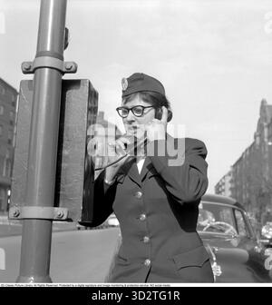 Chauffeur de taxi féminin dans les années 1950 Dans les années 1950 et 1960, les chauffeuses de taxi étaient une présence rare mais frappante sur les routes. Défiant les normes de genre, ces femmes ont navigué dans des villes animées, offrant un service vital avec confiance et compétence. Dans les années 1950 et 1960, les téléphones de station de taxis, montés sur des poteaux où les taxis attendaient, permettaient aux chauffeurs de recevoir des réservations directement d'une répartition centrale. Les clients pouvaient appeler le numéro du rang, et la cloche du téléphone alerterait les conducteurs, assurant des réponses rapides dans les zones urbaines achalandées. Photo Harriet Jonsson au téléphone avec un client directement ou avec le répartiteur de taxi. Banque D'Images