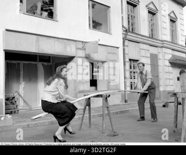 Signe Hasso (1915-2002), actrice et écrivaine suédoise, avec Alf Kjellin (1920-1988), photographiée lors du tournage de This Can't Happen Here (suédois : Sånt händer inte här) en 1950. Ils sont assis sur ce qui ressemble à une balançoire, profitant d'un moment léger lors d'une pause dans le tournage. Hasso a commencé sa carrière sur la scène suédoise avant de déménager à Hollywood dans les années 1940, où elle est apparue dans des films aux côtés de stars comme Spencer Tracy et William Powell. Elle est devenue plus tard une auteure et traductrice respectée. Réf. : I1175 Banque D'Images