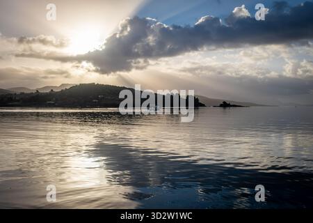 Paysage marin de l'aube d'automne avec la lumière du soleil brisant à travers les nuages pour projeter des reflets sur la mer calme. Banque D'Images