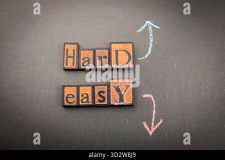 Blocs en bois orthographiant dur et facile avec des flèches de craie sur fond sombre. Symbolisant la difficulté, la décision et les défis de la vie. Banque D'Images