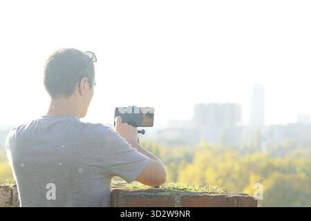 Homme filmant des vidéos personnelles à l'extérieur en utilisant la configuration trépied de smartphone. Représente le mode de vie nomade numérique, l'entrepreneuriat créatif, l'état d'esprit des influenceurs. Banque D'Images