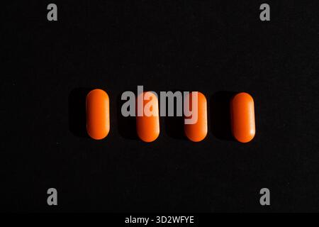 Quatre pilules orange alignées sur fond noir Banque D'Images