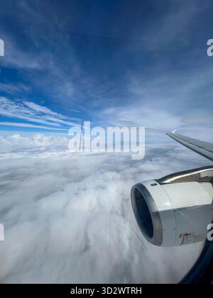 Vue depuis une fenêtre d'avion montrant le moteur à réaction et l'aile volant haut au-dessus des nuages blancs moelleux sous un ciel bleu vif. Banque D'Images