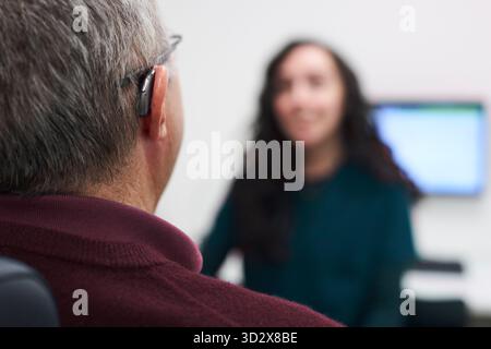 Gros plan d'un homme mature avec un appareil auditif ayant une consultation avec une audiologiste féminine Banque D'Images