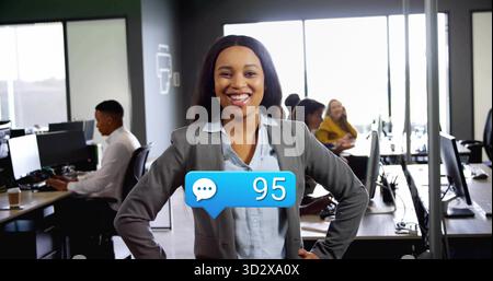 Femme confiante debout dans Blazer menant le travail d'équipe dans un bureau ouvert, avec des moniteurs Banque D'Images