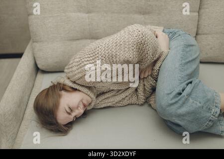 Jeune femme souffrant de douleurs abdominales à l'estomac allongé sur un canapé Banque D'Images