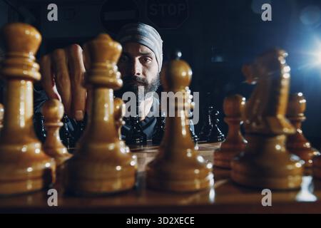 Jeune homme beau adulte jouant aux échecs dans l'obscurité. Figures d'échecs et visage masculin à bord Banque D'Images