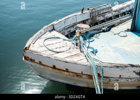 Gros plan d'un ancien bateau de pêche rustique en bois avec des cordes et de l'usure, ancré dans l'eau calme Banque D'Images