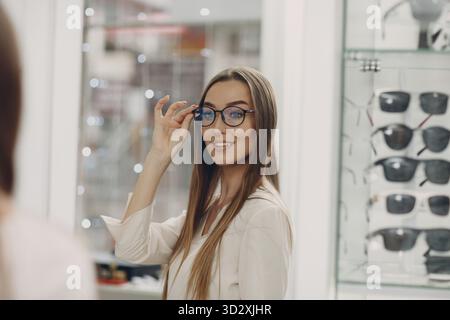 Gros plan de la magnifique jeune femme souriant cueillant et choisissant des lunettes au coin opticien du centre commercial. Bonne femme à l'achat de lunettes Banque D'Images