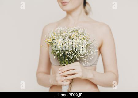 Jeune et belle femme blonde avec bouquet de camomille. Concept de cosmétiques écologiques naturels Banque D'Images