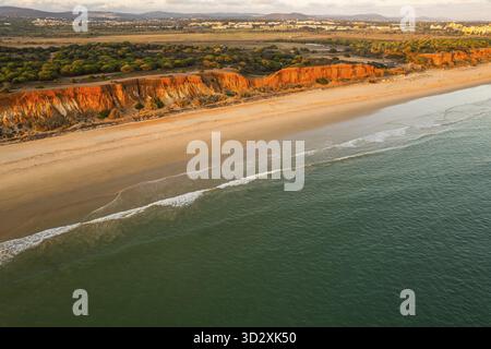 Algarve, côte portugaise avec plage de sable, vagues de l'océan Atlantique et falaises rouges au coucher du soleil. Vue aérienne par drone, Portugal Banque D'Images