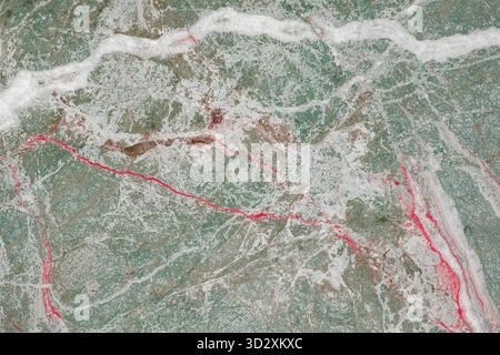 Cette photographie aérienne capture une surface de marbre vert avec des stries rouges proéminentes qui la traversent. Les motifs complexes et les couleurs créent un visuel Banque D'Images
