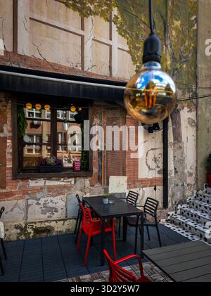 Un café en plein air confortable sur la rue Skadarska à Belgrade, Serbie, avec des chaises rouges et noires, une ampoule suspendue, des murs rustiques décorés d'arbres peints, Banque D'Images