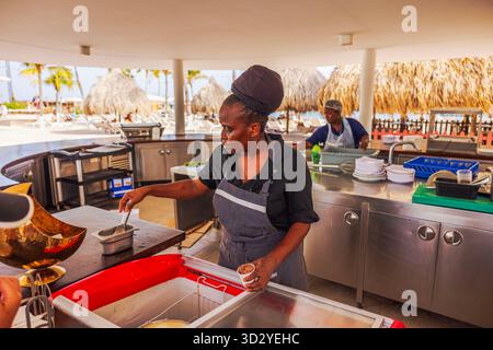 Travailleuse servant de la crème glacée au bar de plage extérieur avec des palmiers et des parasols de paille dans les Caraïbes. Curaçao. Willemstad. Banque D'Images