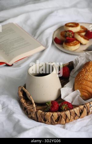 Petit déjeuner confortable au lit avec café, fraises et pâtisseries - atmosphère chaude du matin et mode de vie lent Banque D'Images