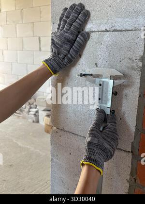 Un ouvrier de la construction utilise un pied à coulisse pour mesurer le diamètre d'une vis. Chantier de construction. Rénovation, nouveau bâtiment. Banque D'Images