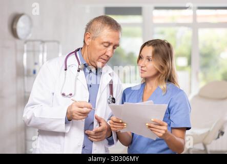 Les médecins hommes âgés et femmes adultes discutent des documents Banque D'Images