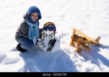 Enfant construisant un bonhomme de neige un jour d'hiver. Enfant heureux roulant de la neige pour faire un bonhomme de neige. Enfant excité jouant avec bonhomme de neige dans la neige fraîche. Enfant mignon Banque D'Images