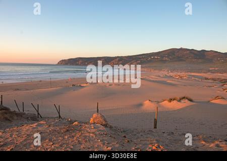 Lumière du soir sur les dunes et les vagues à Praia do Guincho près de Cascais, avec les collines du parc naturel de Sintra-Cascais en arrière-plan Banque D'Images