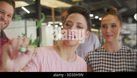 Femme mature portant un panneau de verre de marquage de pull rose dans un bureau ouvert moderne, avec un marqueur vert Banque D'Images