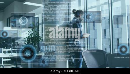 Tenant smartphone sweat à capuche homme collaborant au bureau avec deux moniteurs et graphiques HUD Banque D'Images