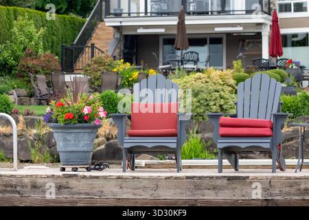 Issaquah, Washington, États-Unis. Deux chaises et un pot plein de fleurs reposant sur un quai à côté d'une maison en bord de lac. Banque D'Images
