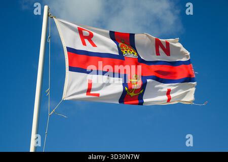 Aberystwyth, pays de Galles, Royaume-Uni - 1er septembre 2025 ; le drapeau de la Royal National Lifeboat institution de la RNLI vole dans un vent fort contre un ciel bleu Banque D'Images