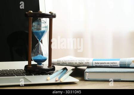 Sablier avec ordinateur portable, livre et journal sur table dans le bureau Banque D'Images