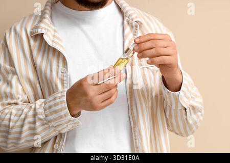 Jeune homme avec bouteille de sérum de vitamine E sur fond beige, gros plan Banque D'Images