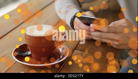 Mains de l'homme tenant smartphone au-dessus de la table au café, avec latte art, superpositions bokeh, espace de copie Banque D'Images