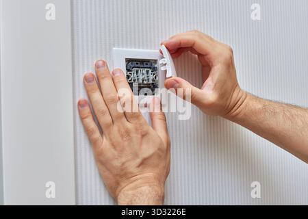mains masculines d'électricien installant un interrupteur d'éclairage électrique blanc à deux touches à la maison. Remplacement. Banque D'Images