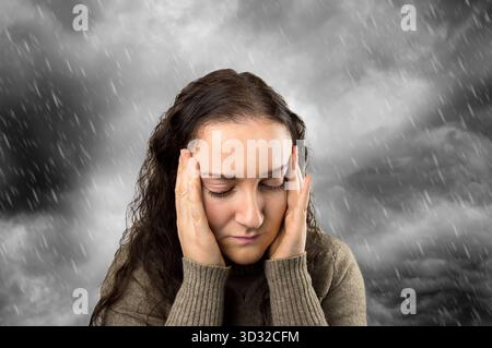 gros plan d'une femme avec mal de tête avec un fond de nuages gris et de pluie Banque D'Images