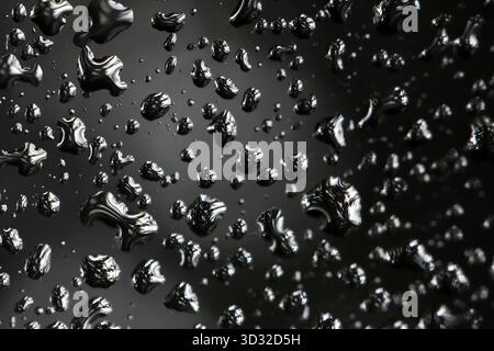 Plan macro mystérieux de gouttelettes de métal liquide brillantes sur une surface noire. Ce fond abstrait a une texture fraîche et humide, parfaite pour la conce de design moderne Banque D'Images