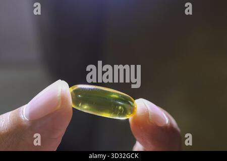 Gros plan de la main d'une femme tenant une seule gélule jaune. Cette image ciblée de supplément vitaminique représente la santé, le bien-être, la nutrition et la personne Banque D'Images