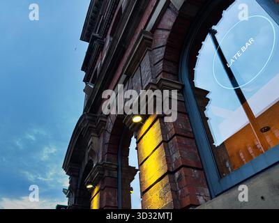 Manchester, Royaume-Uni - 29 septembre 2025 : façade historique en briques avec fenêtres cintrées et éclairage chaleureux du bar à Manchester au crépuscule. Banque D'Images