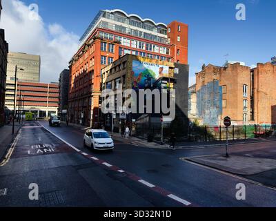 Manchester, Royaume-Uni - 29 septembre 2025 : rue animée de Manchester avec architecture en brique Transmute Studio, art mural et circulation légère par une journée ensoleillée. Banque D'Images