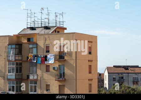 Les vêtements sèchent à la lumière du soleil sur les balcons d'un immeuble jaune à Catane. L'image montre une tranche de la vie quotidienne sicilienne authentique sous un c Banque D'Images