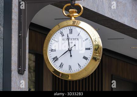 Une horloge dorée de style montre de poche de marque Bucherer suspendue à l'extérieur d'un bâtiment Banque D'Images