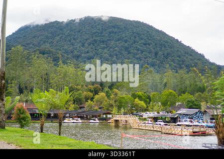 Une vue panoramique sur une montagne verdoyante et densément boisée s'élevant majestueusement au-dessus d'un lac calme avec de petits bâtiments de villégiature. Banque D'Images