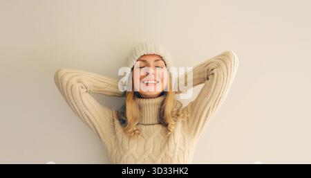 Portrait de détendue jouissant d'une femme souriante heureuse avec les yeux fermés dans des vêtements d'hiver tricotés doux et chauds, pull et chapeau sur fond beige || modèle libéré Banque D'Images