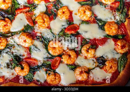 Pizza aux crevettes, tomates et épinards, gros plan. Fond méditerranéen de texture de pizza. Photo de haute qualité Banque D'Images