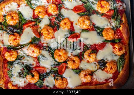 Pizza aux crevettes, tomates et épinards, gros plan. Fond méditerranéen de texture de pizza. Photo de haute qualité Banque D'Images