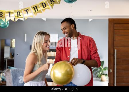 Homme et femme afro-américains tenant des ballons, célébrant l'anniversaire à l'intérieur, souriant. Célébration, bonheur, fête, divers, joyeux, festive || autorisation du modèle Banque D'Images