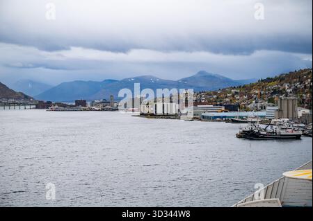 Tromso, Norvège, port avec bâtiments industriels et bateaux, sur fond montagneux sous un ciel nuageux Banque D'Images