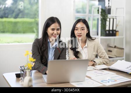 Deux femmes d'affaires collaborant et analysant des données sur un ordinateur portable, discutant des idées dans un environnement de bureau lumineux Banque D'Images