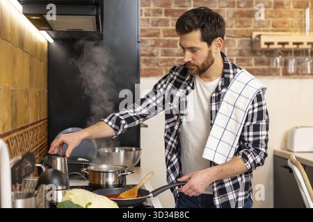 Bel homme barbu préparant le dîner dans la cuisine à la maison Banque D'Images