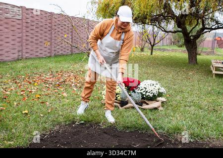 Femme jardinière ratissant le sol dans le jardin d'automne préparant le terrain pour planter des fleurs Banque D'Images